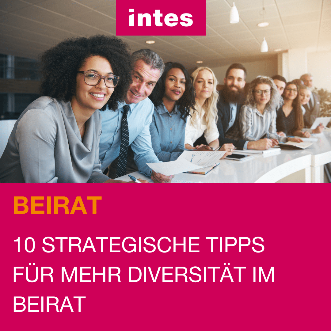 Eine diverse Gruppe von Menschen an einem langen Bürotisch lächeln in die Kamera.