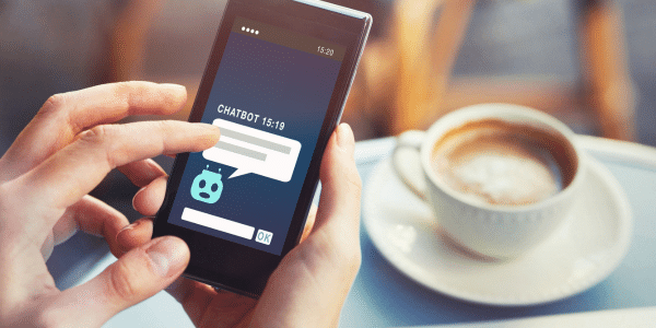 Ein Smartphone auf dem ein Chatbot -Gespräch zu sehen ist, mit einer Tasse Kaffee im Hinterngrund.